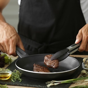person cooking meat in nonstick skillet herbs on counter