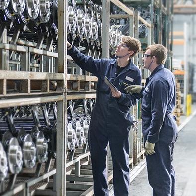two men looking at rows of stored car axles on a shelving unit at a car plant