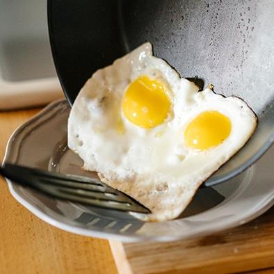 two sunnyside up eggs sliding from a frying pan onto a plate