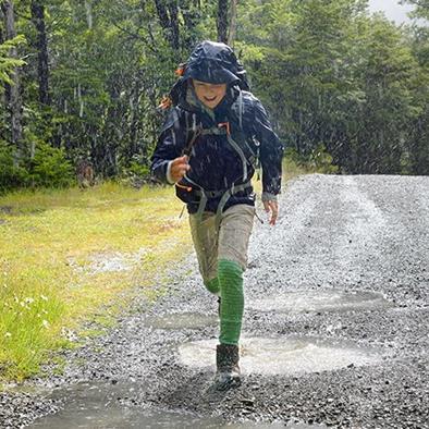 young boy wearing blue jacket running through the rain and smiling