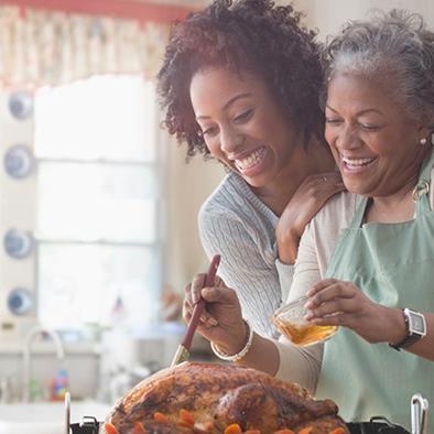 younger woman hugging older woman whos basting a turkey