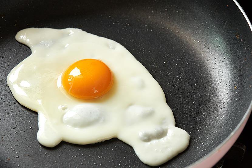 closeup of sunnyside up egg cooking in a frying pan