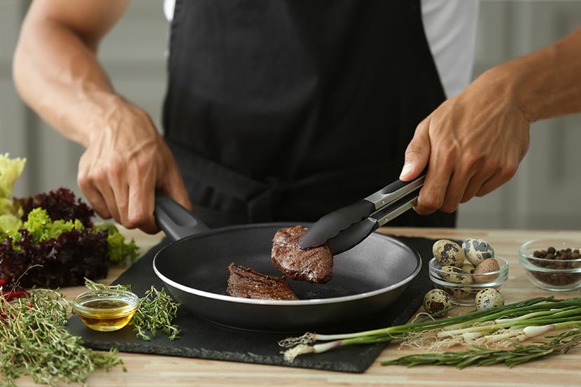 person cooking meat in nonstick skillet herbs on counter 