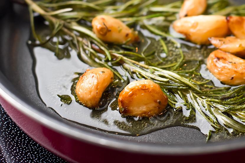 garlic cloves and rosemary sauteing in oilve oil in a frying pan