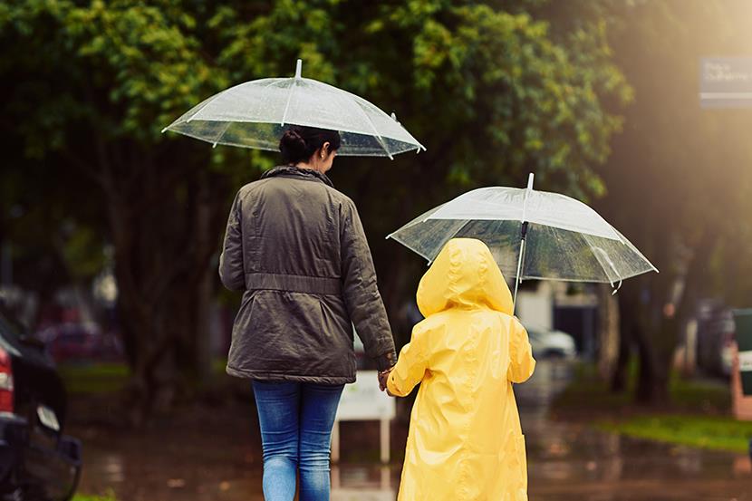 mother and child wearing raincoat are holding hands umbrellas walking through the rain