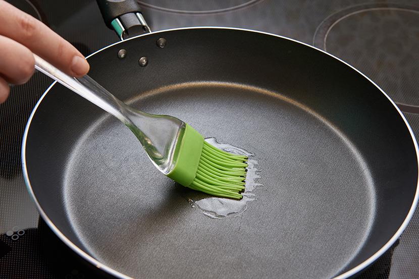 person using a basting brush to brush oil into a frying pan