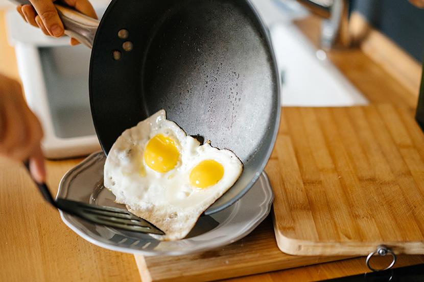 two sunnyside up eggs sliding from a frying pan onto a plate