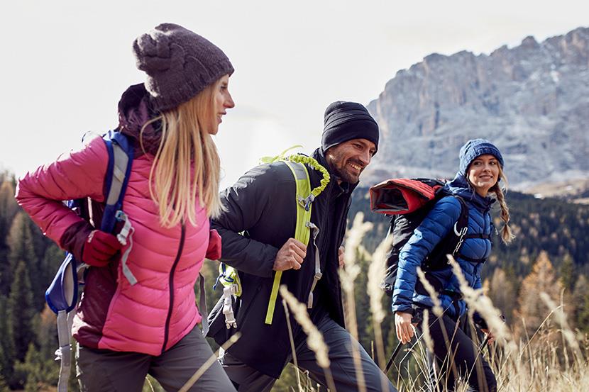 two women and man wearing jackets hiking in mountains