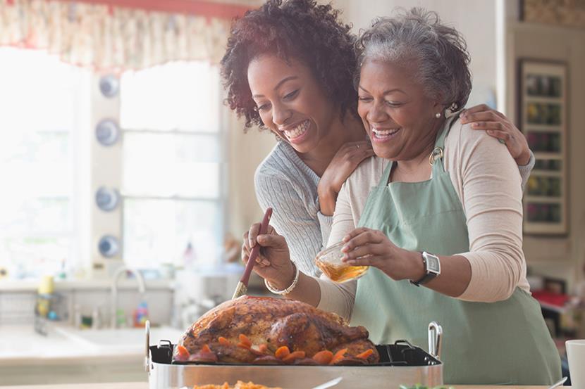 younger woman hugging older woman whos basting a turkey
