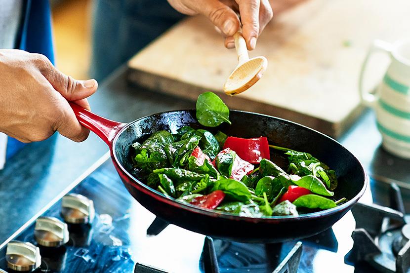 person sauteing spinach and red peppers in a skillet